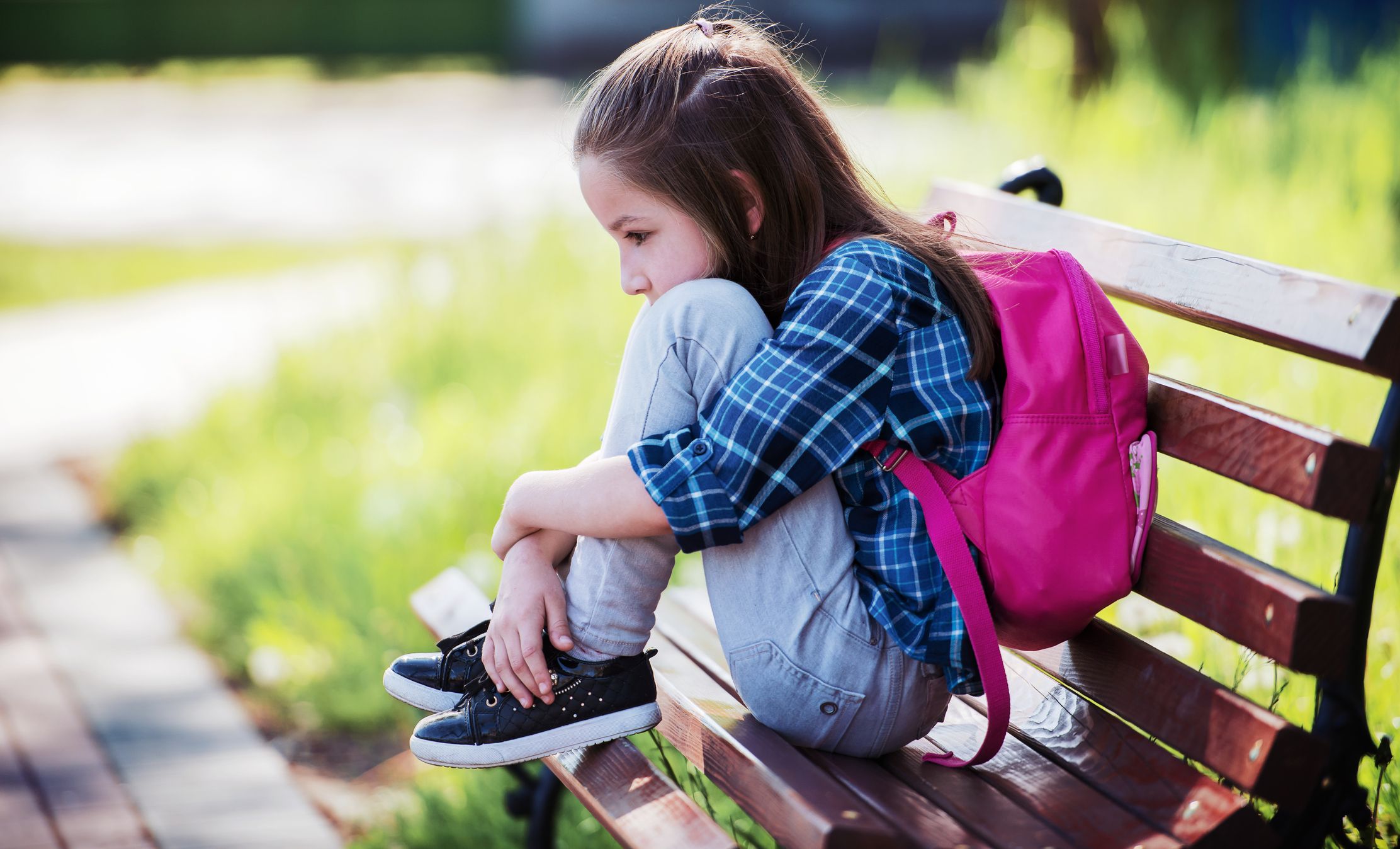 upset school aged girl sitting on a bench